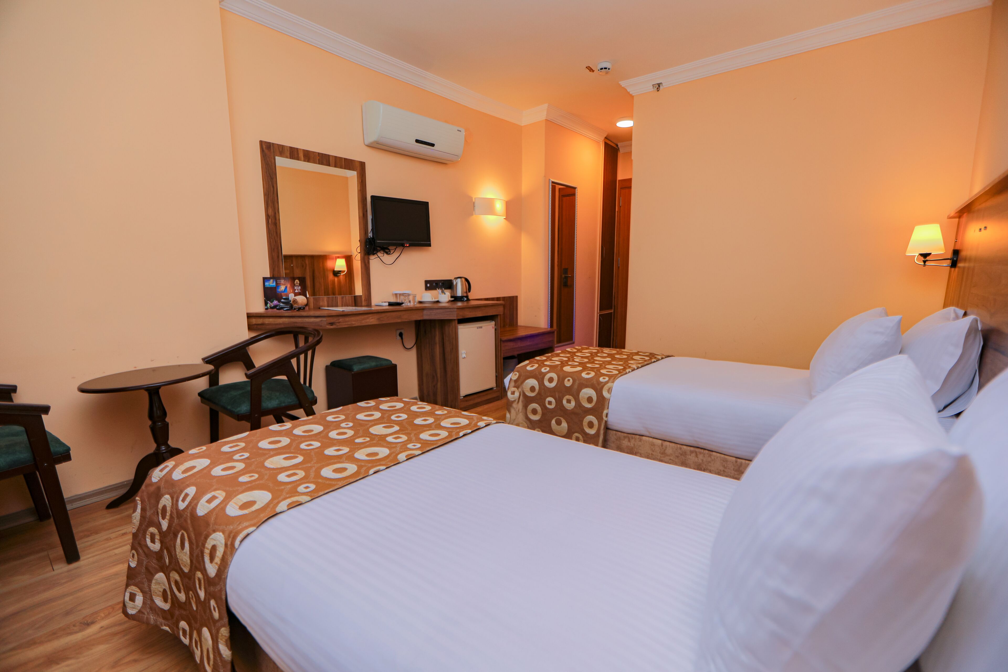 A hotel room with two beds, a desk with a chair, a television, and a coffee machine.