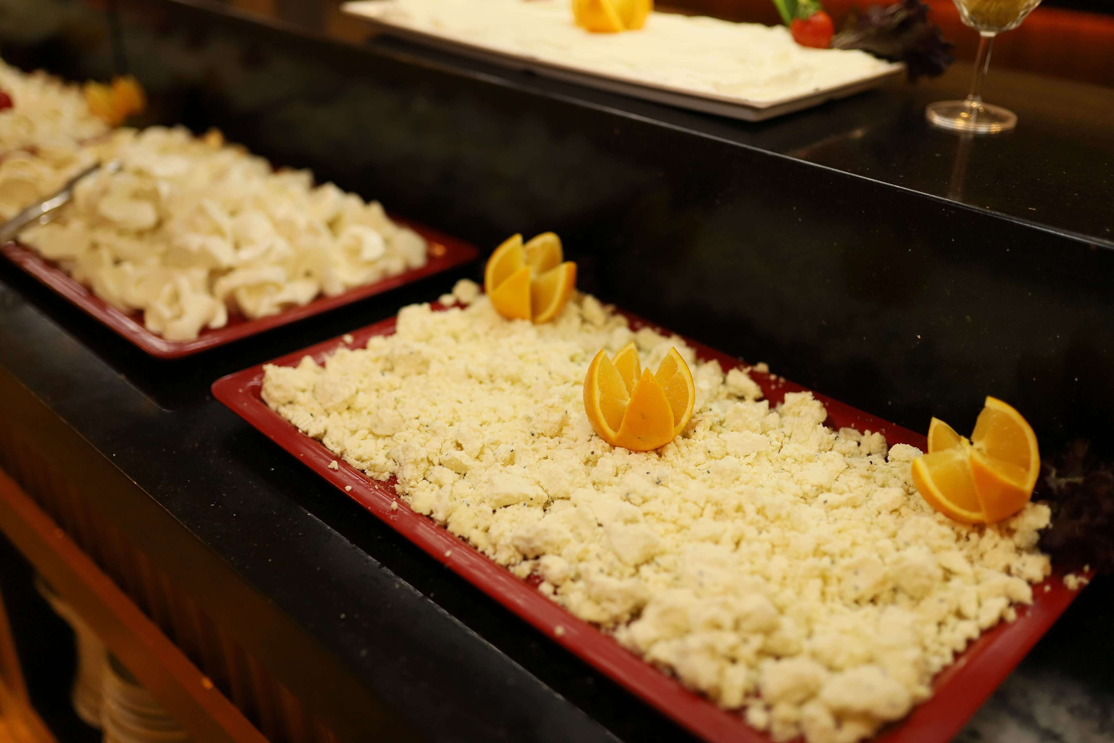 A buffet table with various dishes, including a dish topped with crumbled cheese and orange slices.