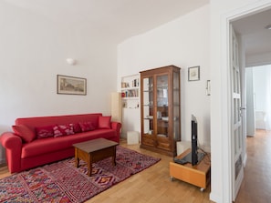 Ein Wohnzimmer mit einem roten Sofa, einem Holzschrank und einem Fernseher auf einem Schrank.