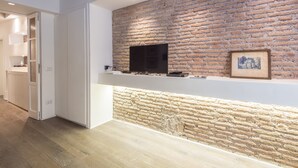 A modern kitchen with exposed brick walls, a built-in TV, and a stone accent wall. - RSH Luxury One Bedroom Fori Imperiali (Rome)
