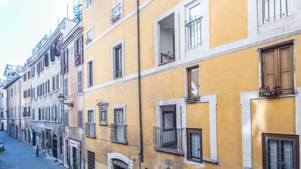 A narrow street lined with yellow buildings, each with multiple windows and balconies. - RSH Luxury One Bedroom Fori Imperiali (Rome)