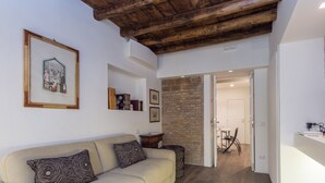 A living room with a beige sofa, patterned cushions, a wooden ceiling, and a brick wall. - RSH Luxury One Bedroom Fori Imperiali (Rome)
