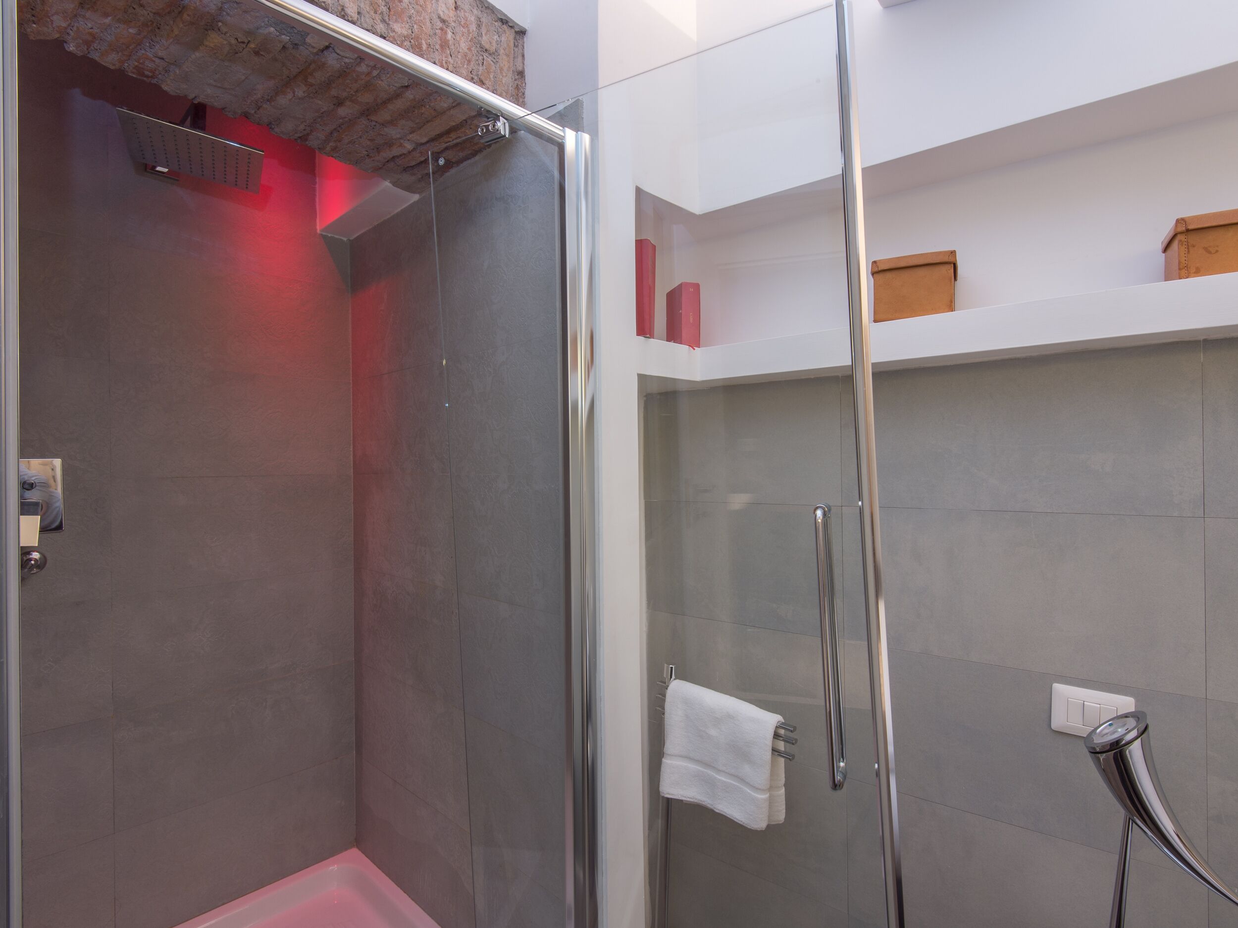 A modern bathroom with a glass shower enclosure, a white towel hanging on a rack, and a red light above the shower.