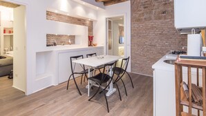 A modern kitchen with a brick wall, white cabinetry, and a wooden ceiling. - RSH Luxury One Bedroom Fori Imperiali (Rome)