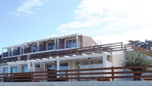 A multi-story building with balconies, a wooden fence in the foreground, and a clear sky. - Affittimoderni Isola Rossa Élite - Pati19 (Trinità d'Agultu e Vignola)