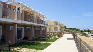A row of modern multi-story buildings with balconies, a paved walkway, and a view of the sea. - Affittimoderni Isola Rossa Élite - Pati19 (Trinità d'Agultu e Vignola)