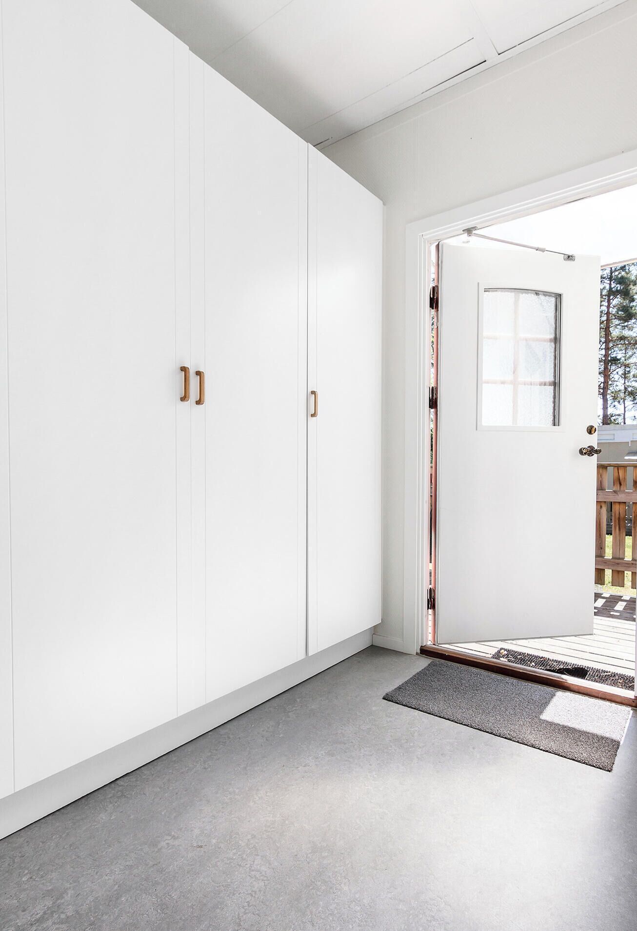 A modern interior with white walls, a grey floor, and a door leading outside.