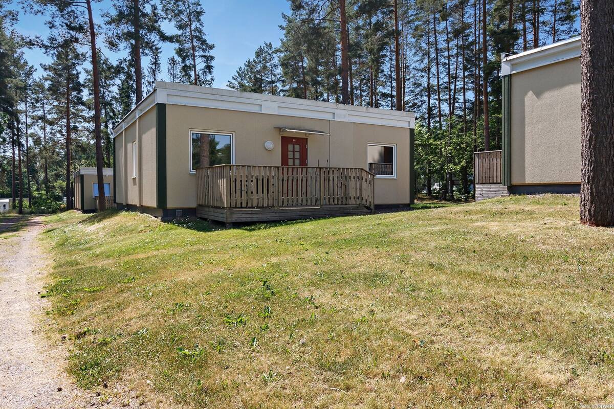 A single-story mobile home with a front porch, surrounded by a forest.