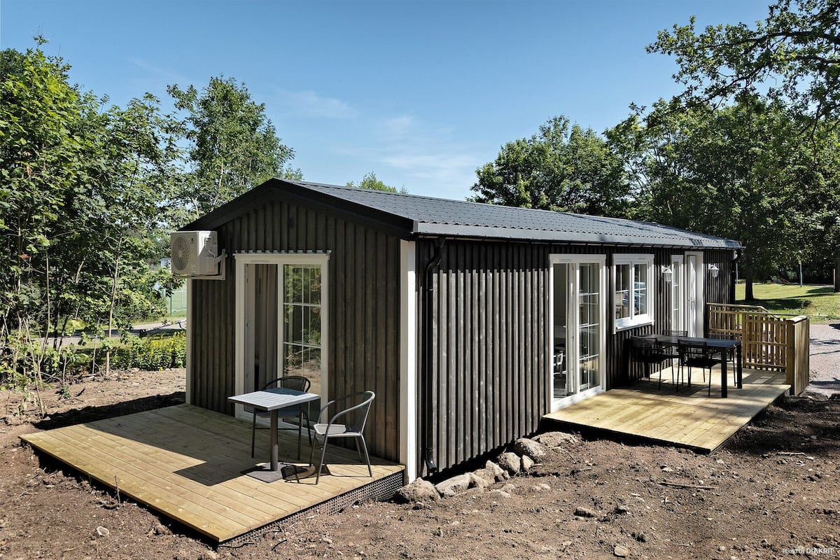 A small wooden cabin with a deck, a table, and chairs.