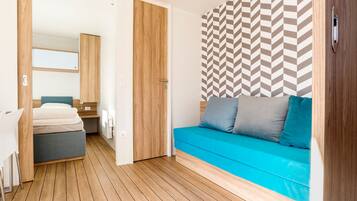 Una habitación moderna con suelo de madera, un sofá azul con cojines, una puerta de madera y una pared con diseño.