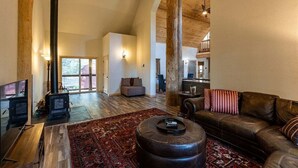 A spacious living room with a large wooden beam ceiling, a fireplace, a leather sofa, and a patterned rug. - Secluded, Spacious, Close to Town, Large Lot, Great Family Home, Hot Tub (Pagosa Springs)