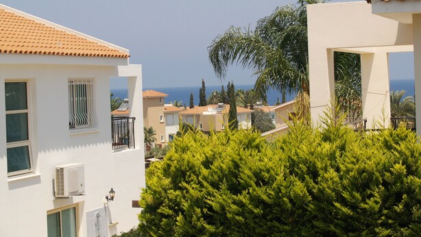 A coastal residential area with white buildings, some with balconies, and a view of the sea. - Villa Nektaria Green Bay DPSV308 (Paralimni)