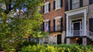 A row of brick townhouses with white trim and black shutters, a flag, and a sign indicating a historical site. - The Sarah Elizabeth House on beautiful Jones St w/ Private Courtyard (Savannah)