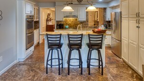A kitchen with three bar stools, a granite countertop, and stainless steel appliances. - The Sarah Elizabeth House on beautiful Jones St w/ Private Courtyard (Savannah)