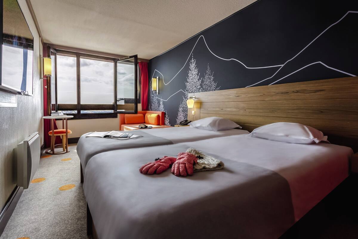 A hotel room with two beds, a wooden headboard, a large window, and a wall mural.