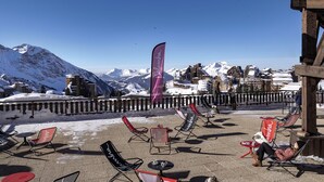 An outdoor seating area with chairs and tables, overlooking a snowy mountain landscape with buildings in the background. - Belambra Clubs Avoriaz - Les Cimes du Soleil  (Morzine)