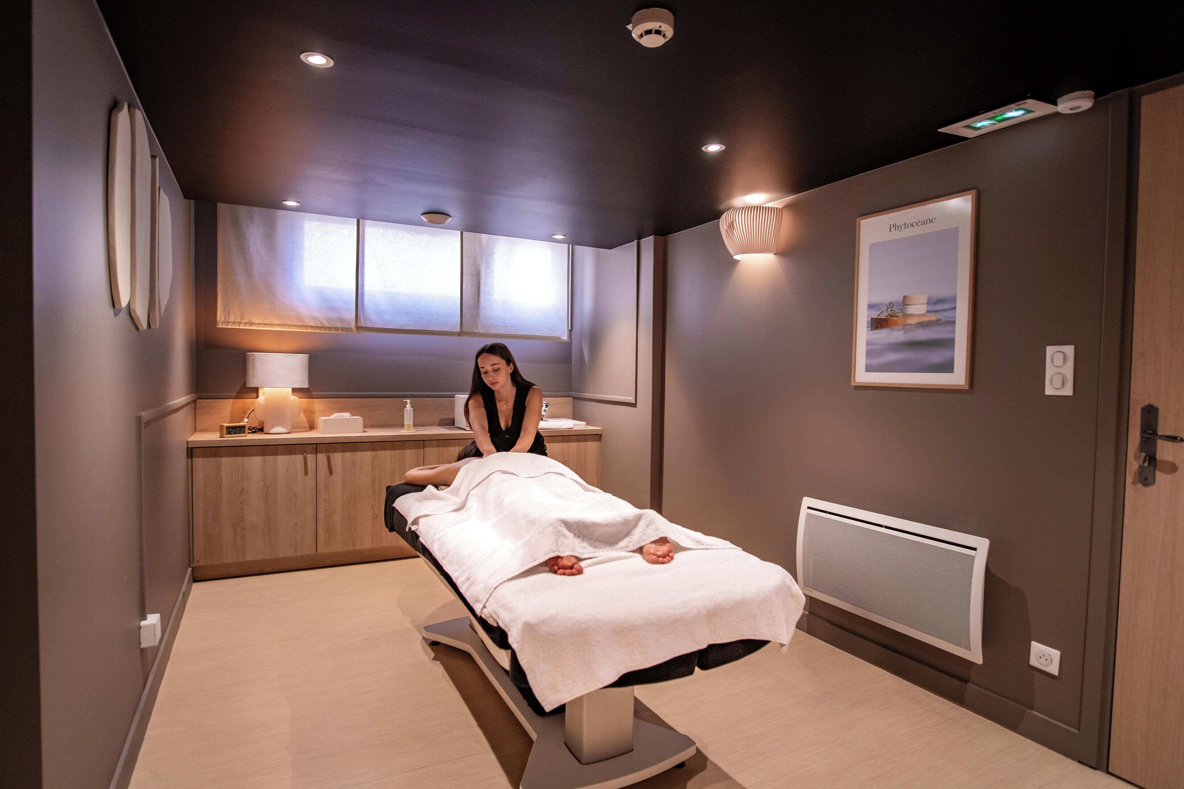 Une pièce moderne équipée d’une table de massage, d’un meuble en bois et d’un fauteuil de massage fixé au mur.