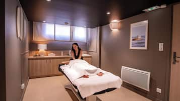 Une pièce moderne équipée d’une table de massage, d’un meuble en bois et d’un fauteuil de massage fixé au mur.