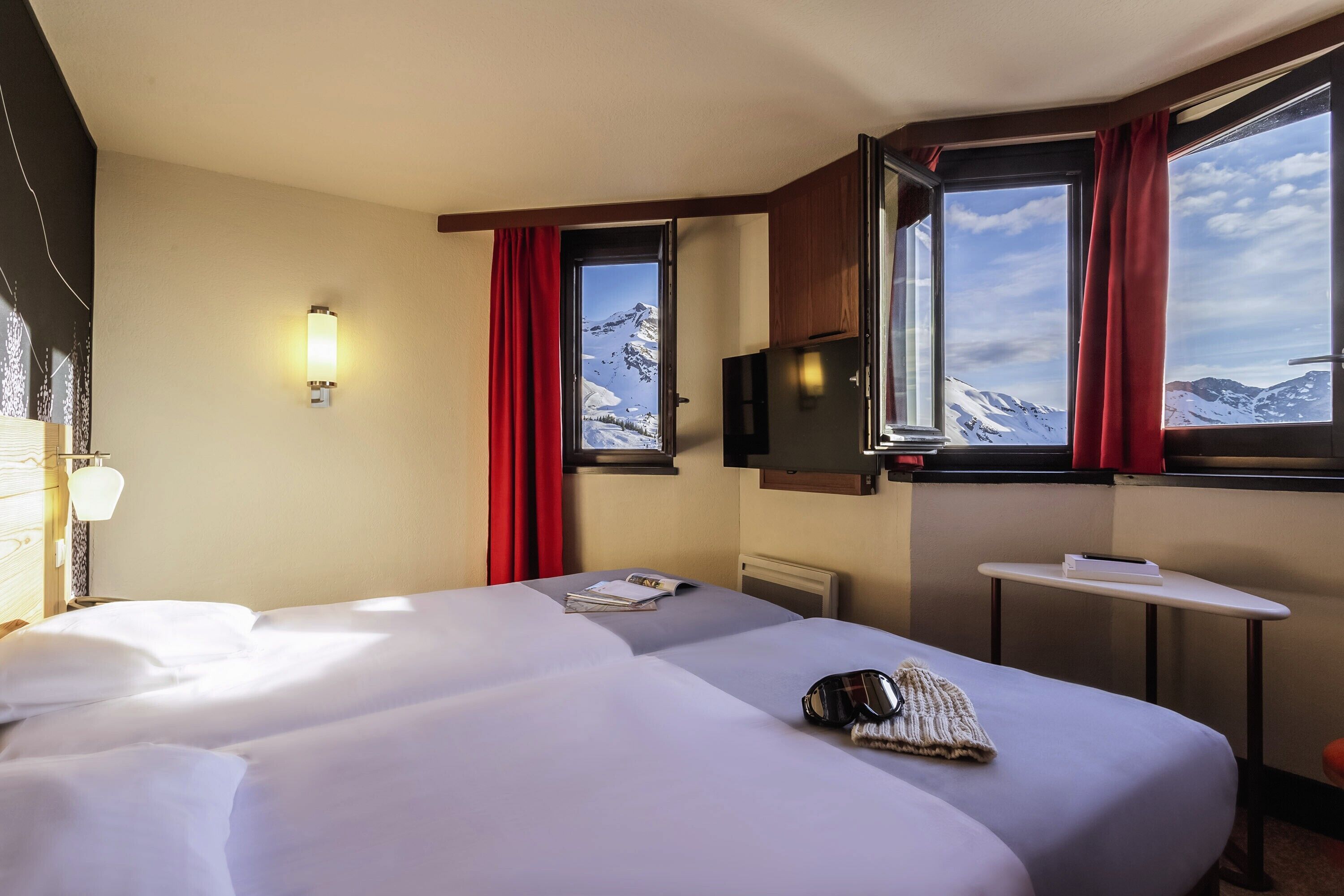 Une chambre d’hôtel avec deux lits, une télévision, une petite table et une fenêtre donnant sur la montagne.