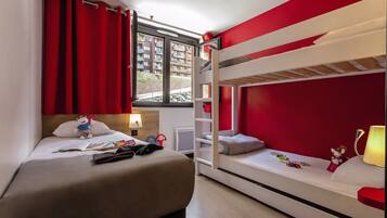 A room with a bunk bed, a desk with a lamp, and a window with red curtains.