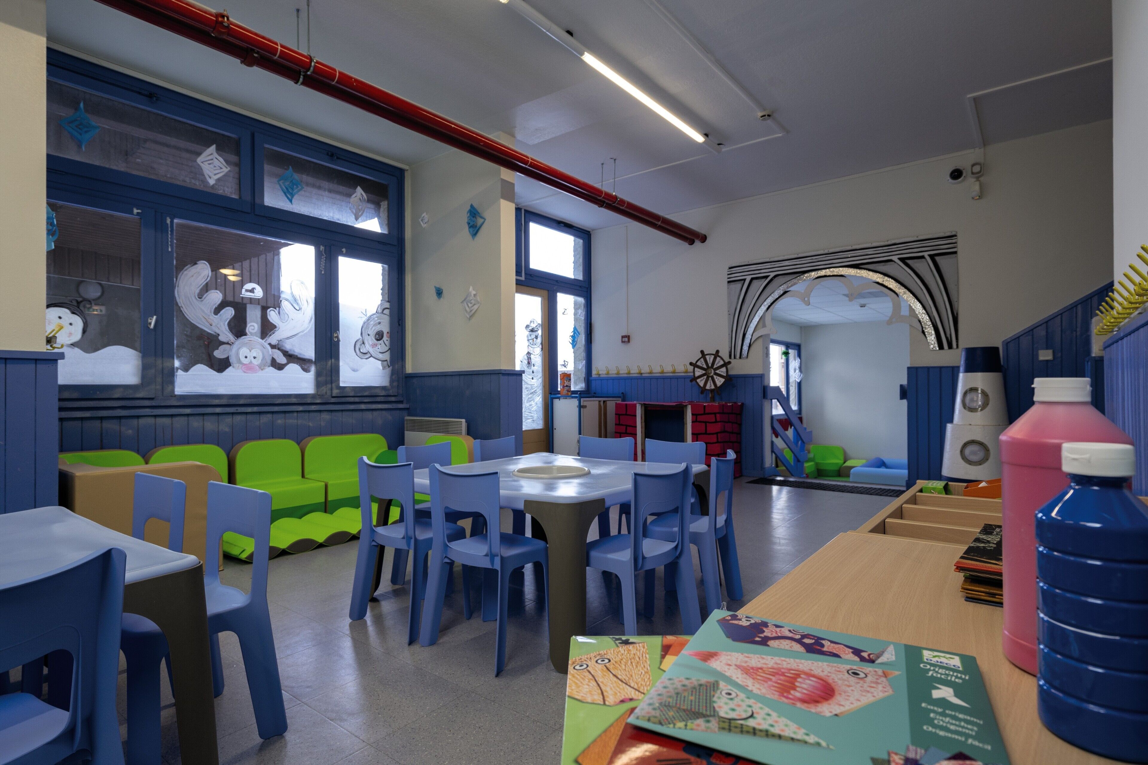 Une salle de classe avec des chaises bleues et vertes, une table ronde et des affiches pédagogiques accrochées aux murs.