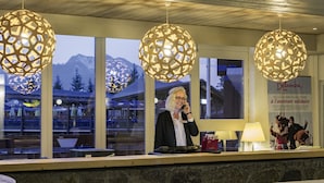 A reception desk with a stone wall, two large spherical hanging lights, and a window with a view of mountains. - Belambra Clubs Arc 1800 - Hôtel Du Golf  (Bourg-Saint-Maurice)