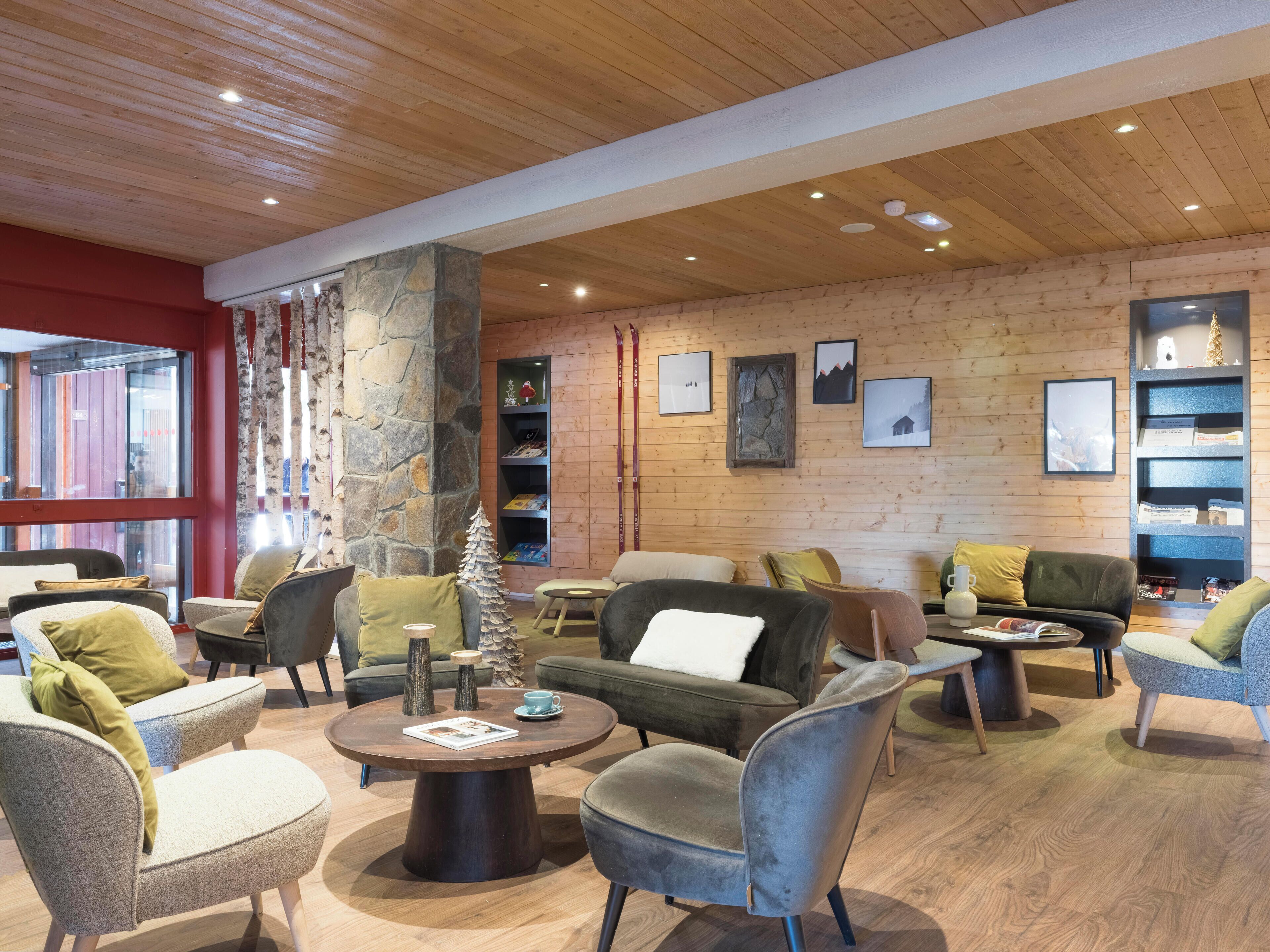 A modern interior with wooden ceilings, stone pillars, and a variety of seating options including sofas and armchairs.