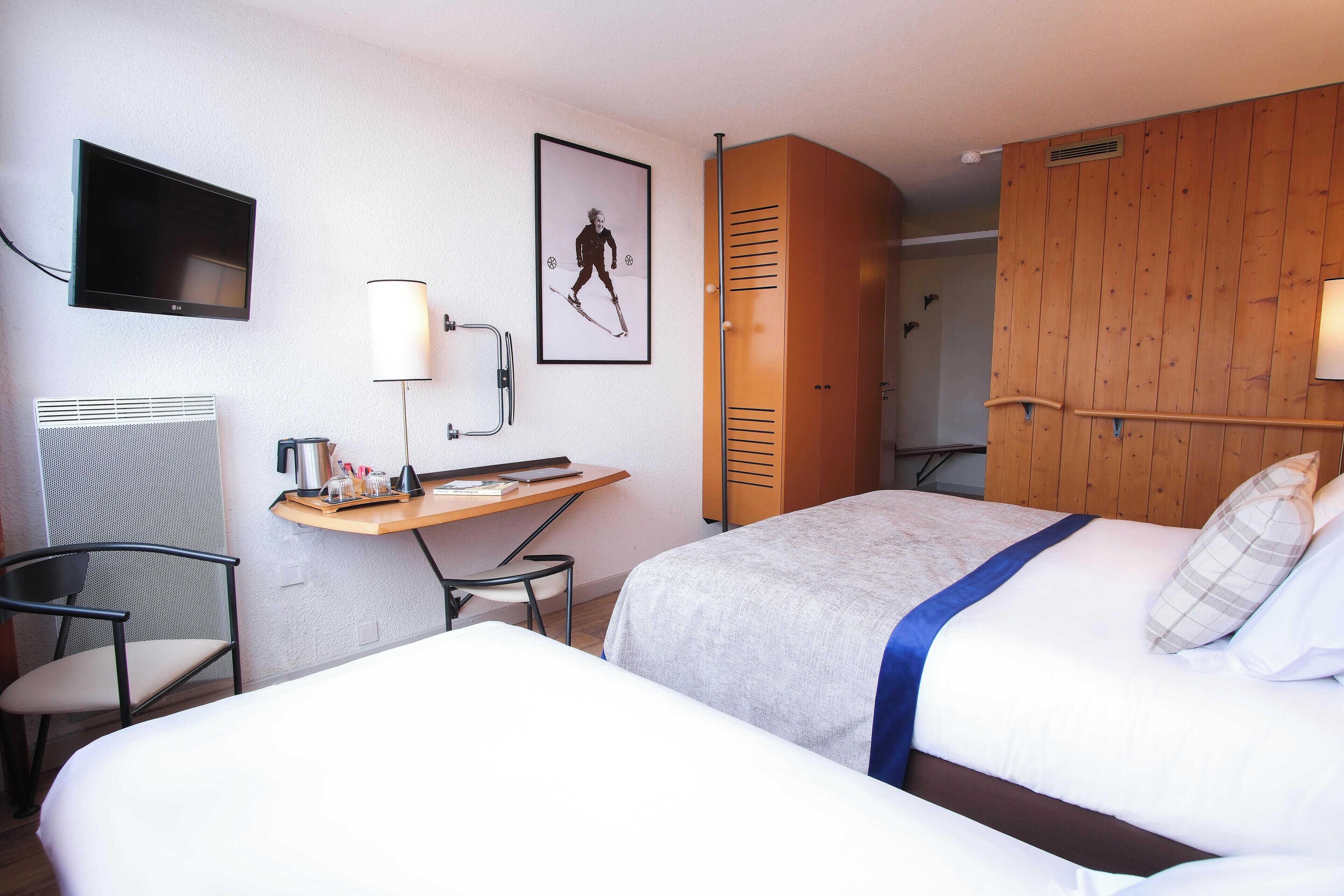 A hotel room with two beds, a desk with a chair, a TV, and a wooden wardrobe.
