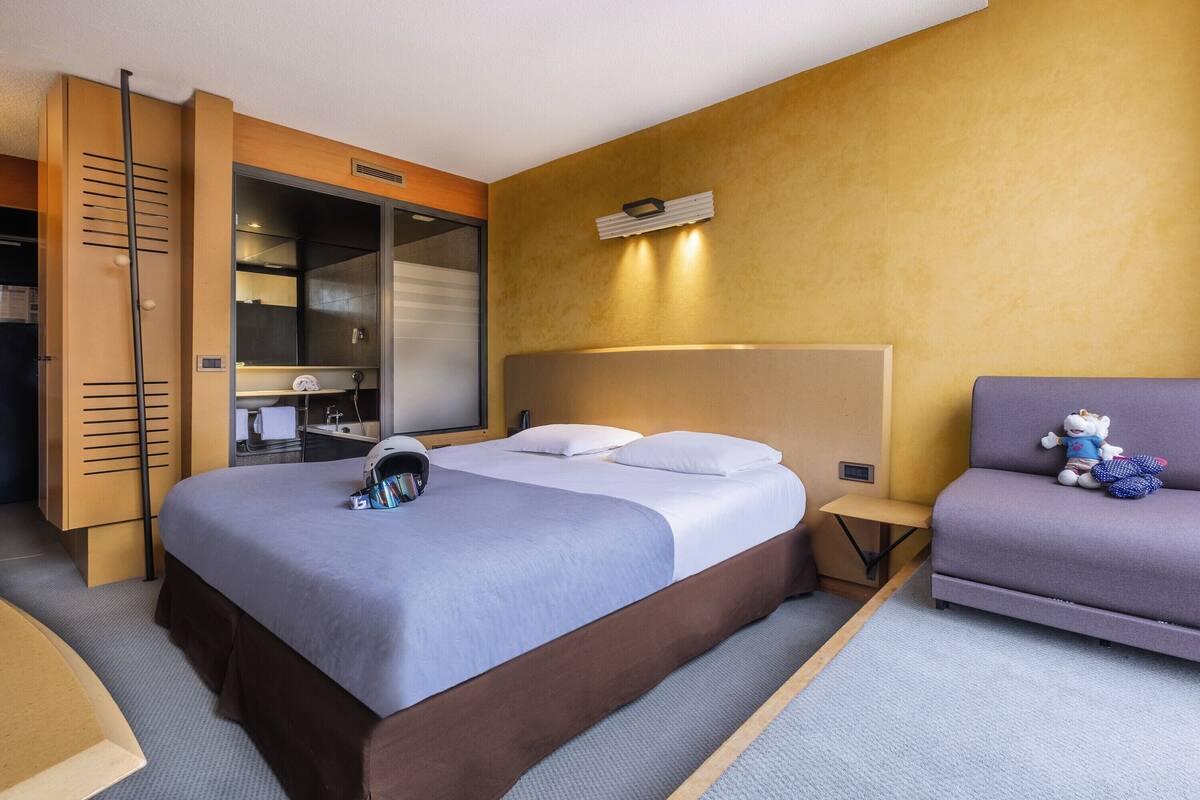 A hotel room with a bed, a sofa, a wardrobe, and a mirror.