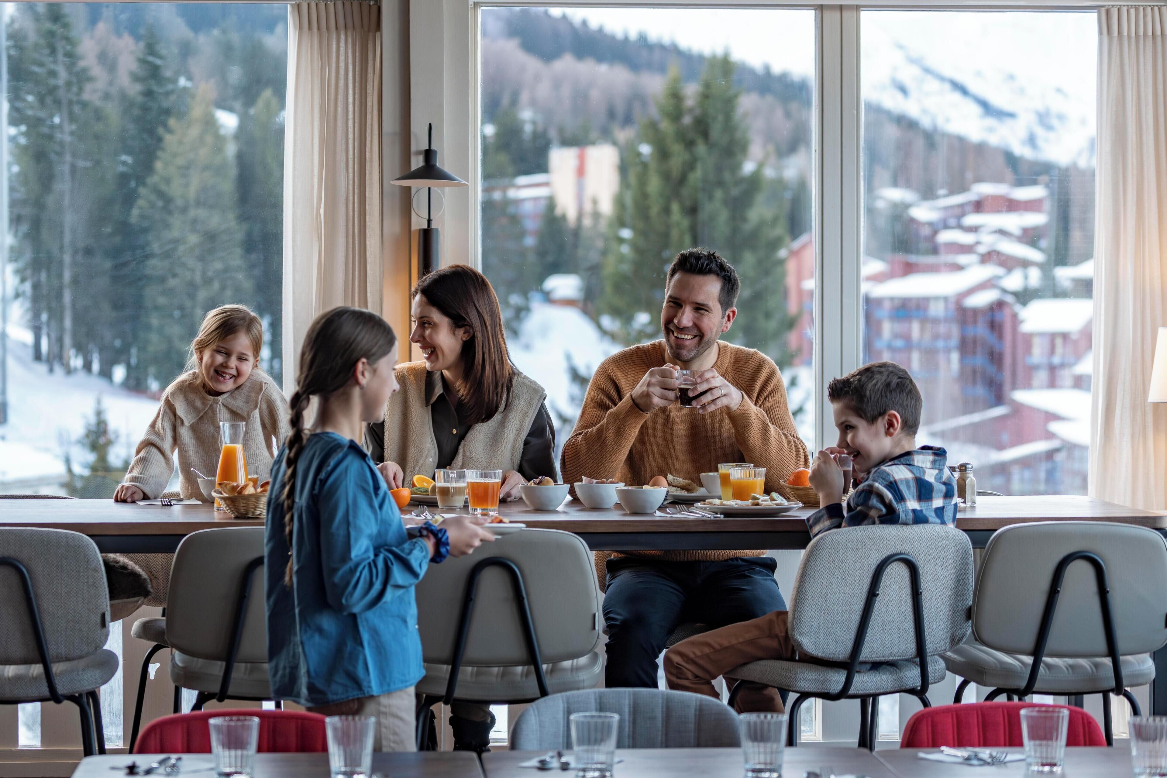 Comedor con mesa dispuesta para una familia, sillas y vista a un paisaje nevado a través de amplias ventanas.