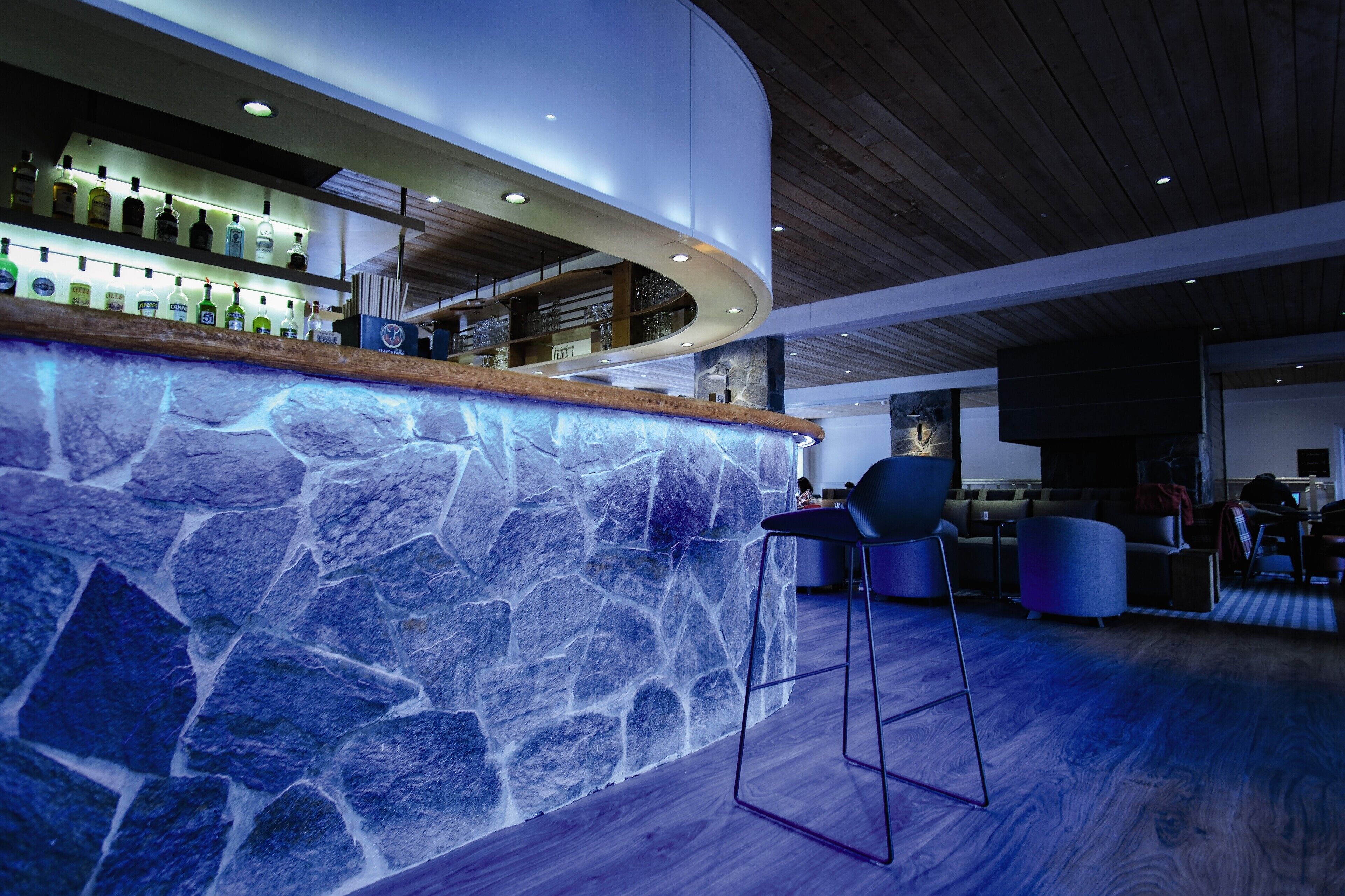 Un espace bar moderne avec un comptoir en pierre, des tabourets de bar et un plafond en bois.
