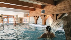 An indoor swimming pool with wooden beams, a water feature, and a tiled wall. - Belambra Clubs Arc 1800 - Hôtel Du Golf  (Bourg-Saint-Maurice)