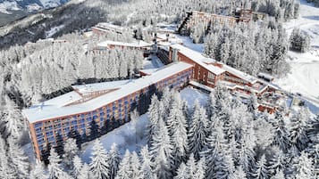 Un grand hôtel à plusieurs étages, doté d’une façade incurvée, entouré d’arbres et de montagnes couverts de neige.