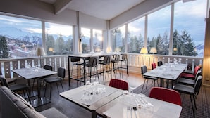 A restaurant with tables set for dining, large windows offering mountain views, and a balcony with a railing. - Belambra Clubs Arc 1800 - Hôtel Du Golf  (Bourg-Saint-Maurice)