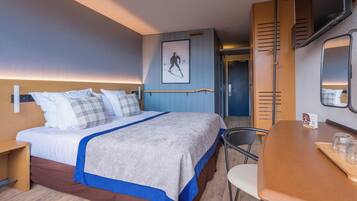 Camera d'albergo con un letto, una scrivania, una sedia, uno specchio, un quadro appeso al muro e una porta che dà su un'altra stanza.