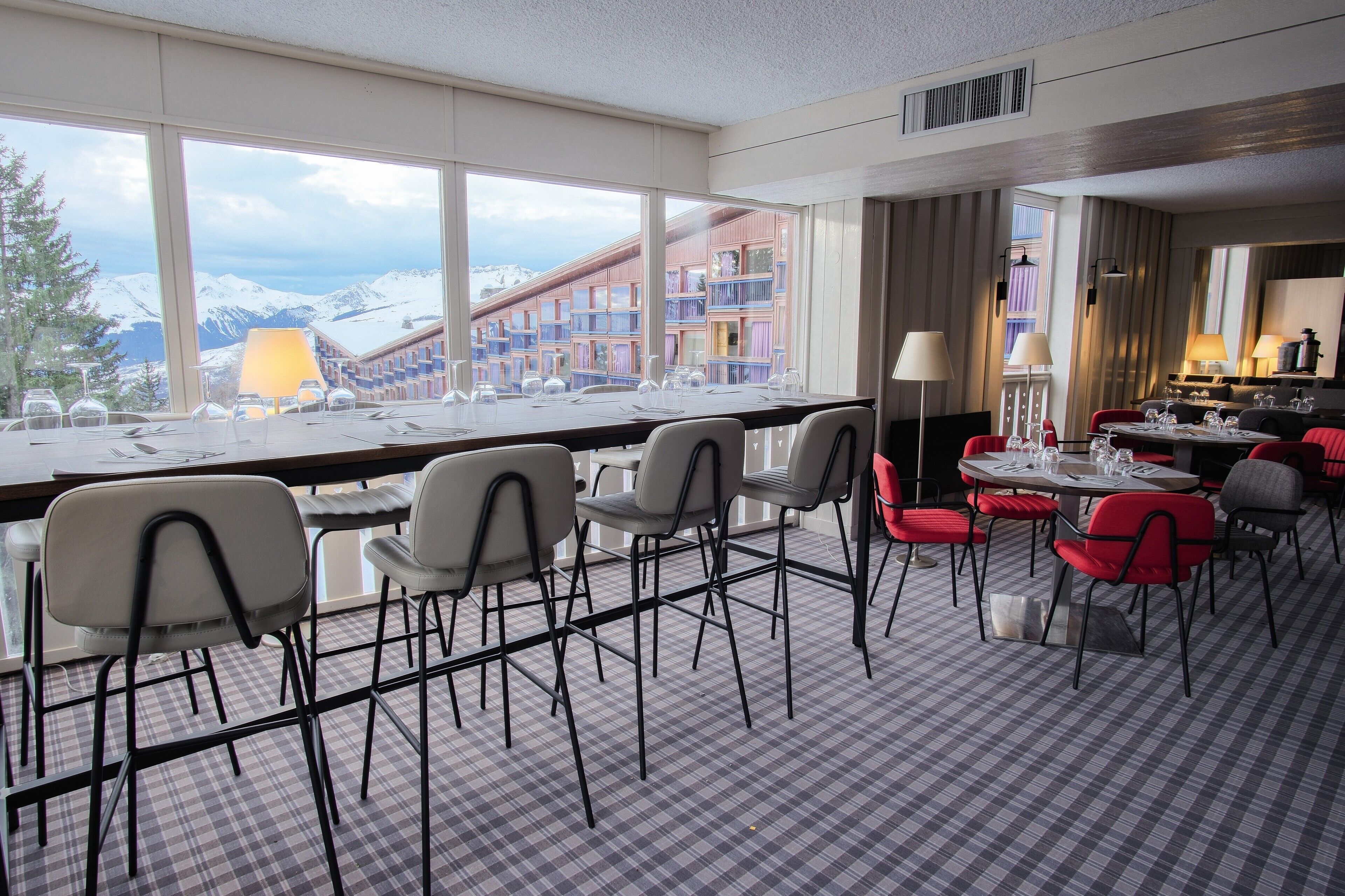 A hotel dining area with a large window view of mountains, a checkered floor, and red and grey chairs.