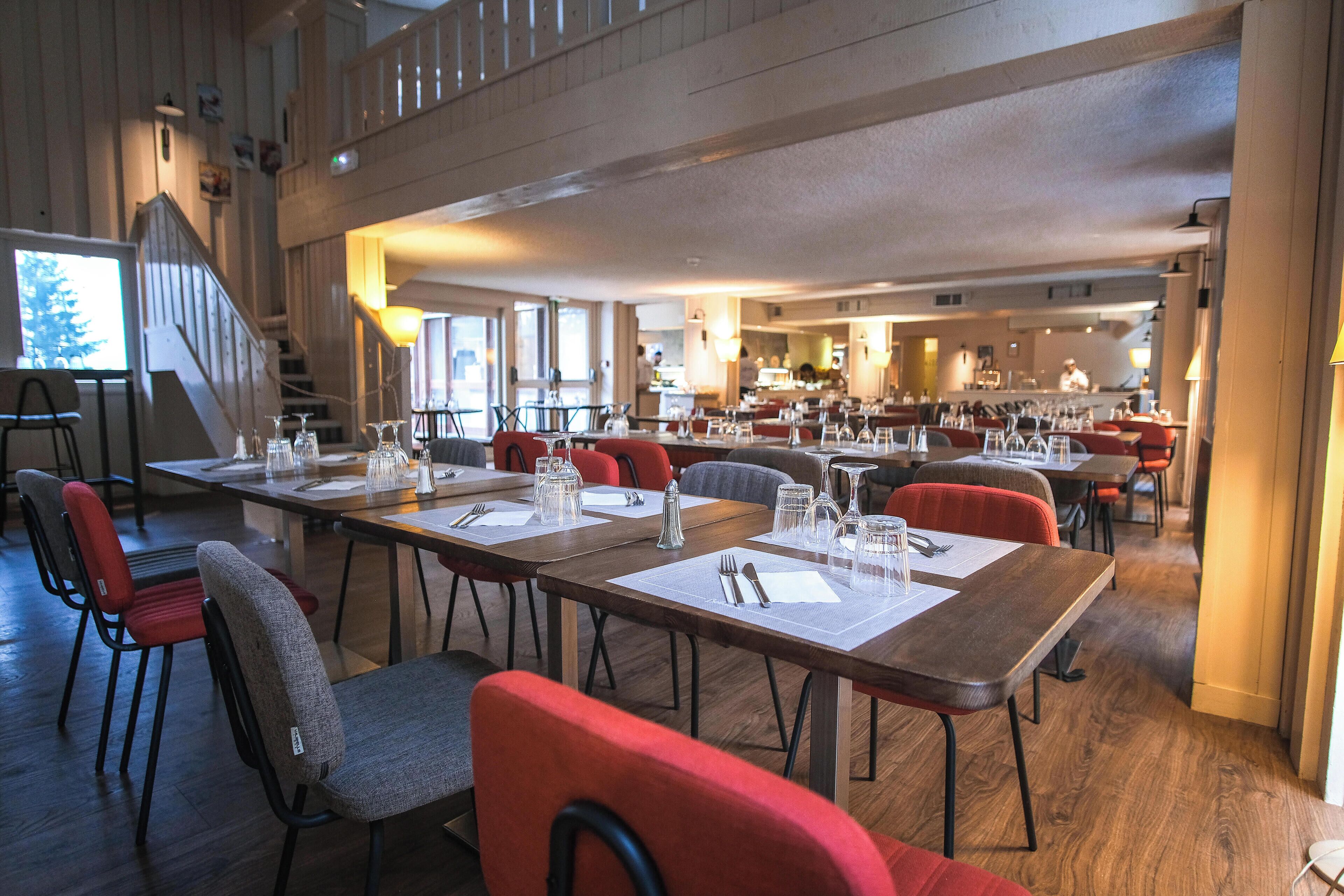 A spacious dining area with multiple tables and chairs, a staircase, and a view of the kitchen area.