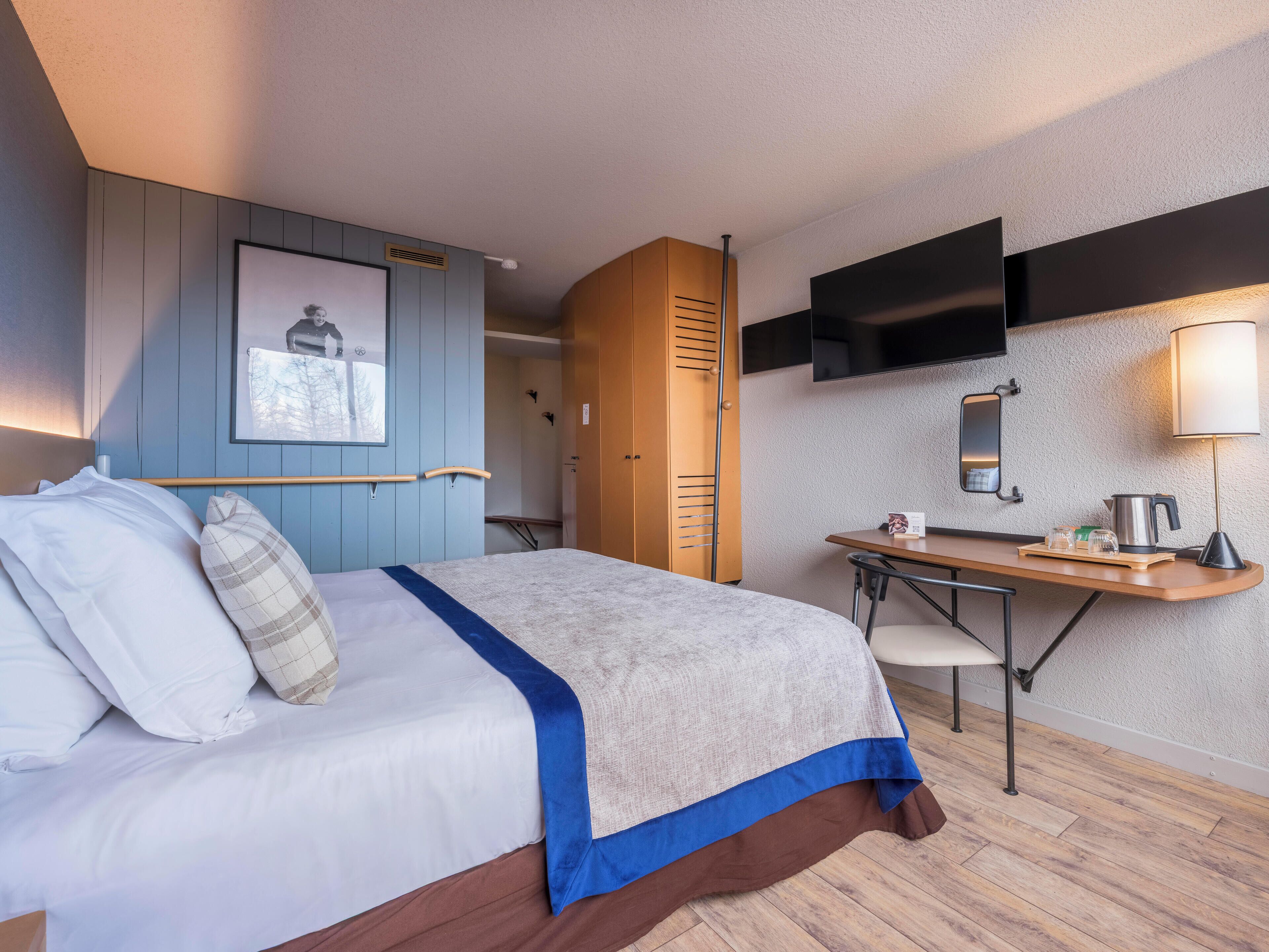 Una habitación de hotel con cama, escritorio, televisor y espejo.