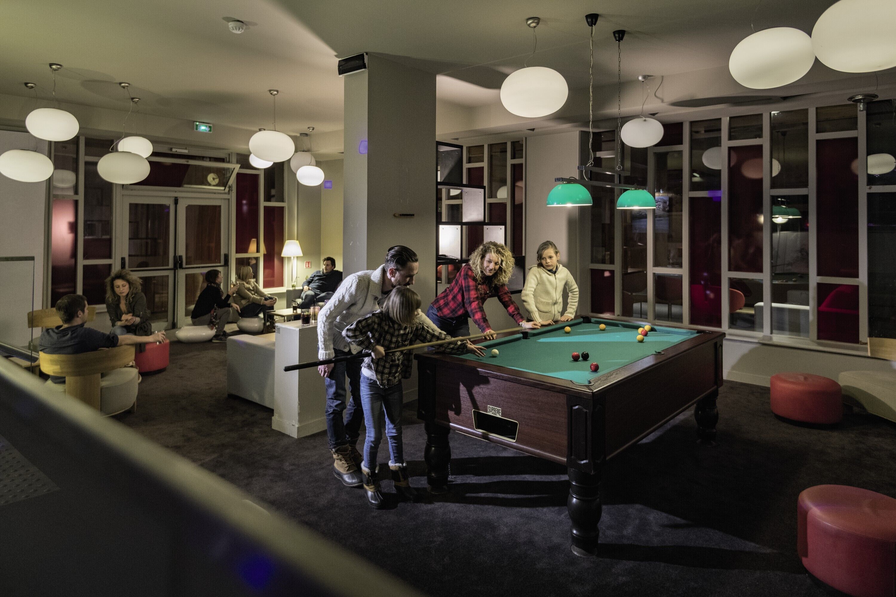 Une table de billard dans une pièce au mobilier moderne, éclairée par des suspensions.