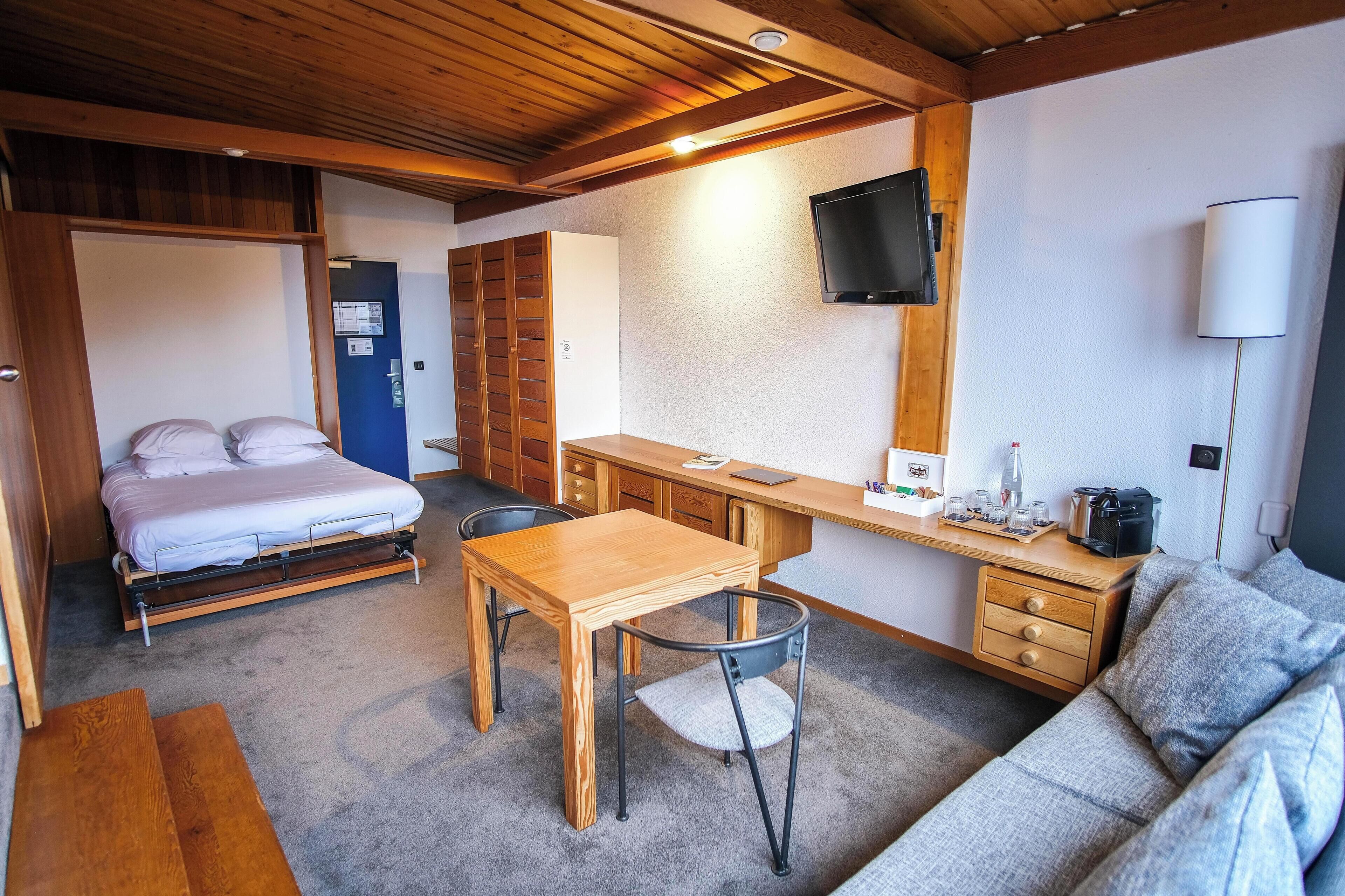 Ein kleines Zimmer mit Bett, Schreibtisch, Stuhl, einer Couch und einem Fernseher.