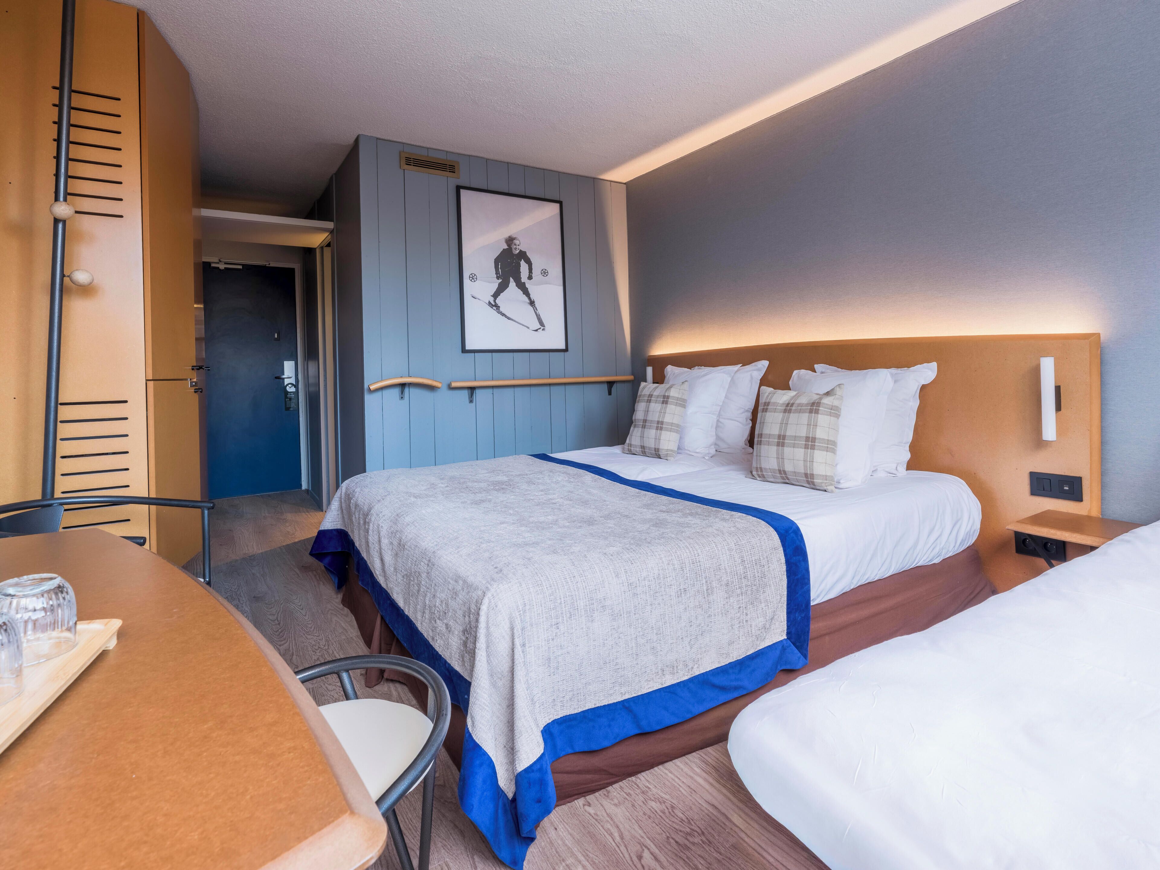 A hotel room with a bed, bedside tables, a desk with a chair, and a framed picture on the wall.