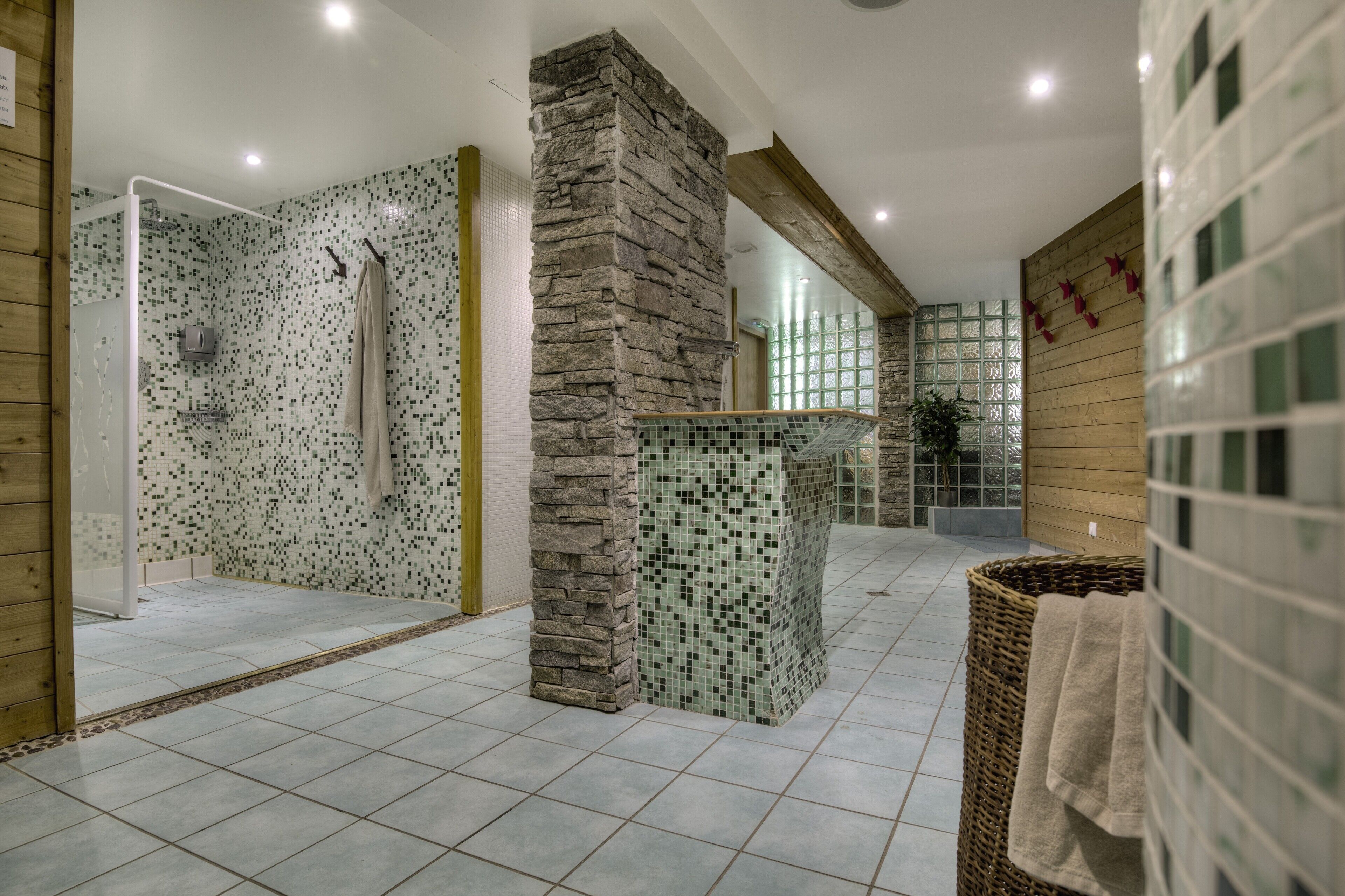A modern bathroom with a shower, tiled walls, a stone pillar, and a tiled floor.