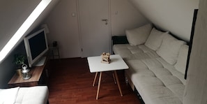 Ett litet, ombonat rum med ett trägolv, en vit soffa, ett litet bord och en tv som står på ett träställ.