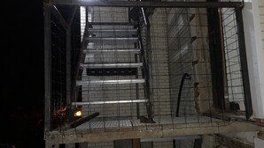 Una escalera metálica que sube a un nivel superior, rodeada de muros de ladrillo y una barandilla metálica.