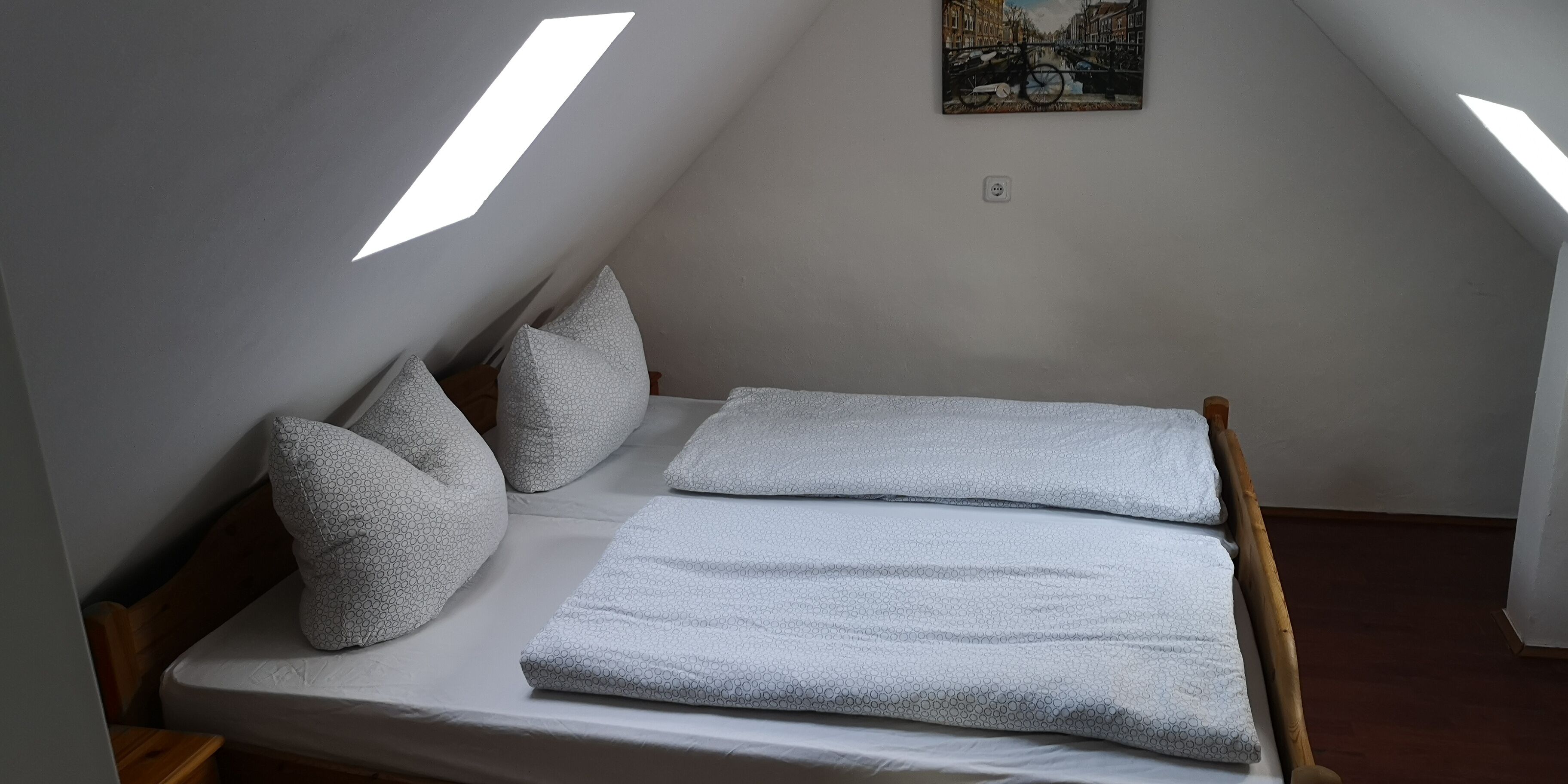 Ein schlichter, kleiner Raum mit einem Bett, Kissen und einem Bild an der Wand.