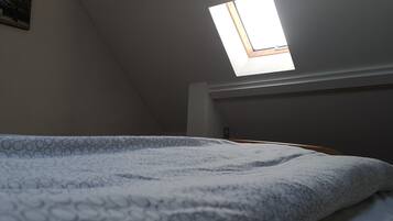 A bedroom with a skylight, a bed with a patterned blanket, and a wall-mounted painting.