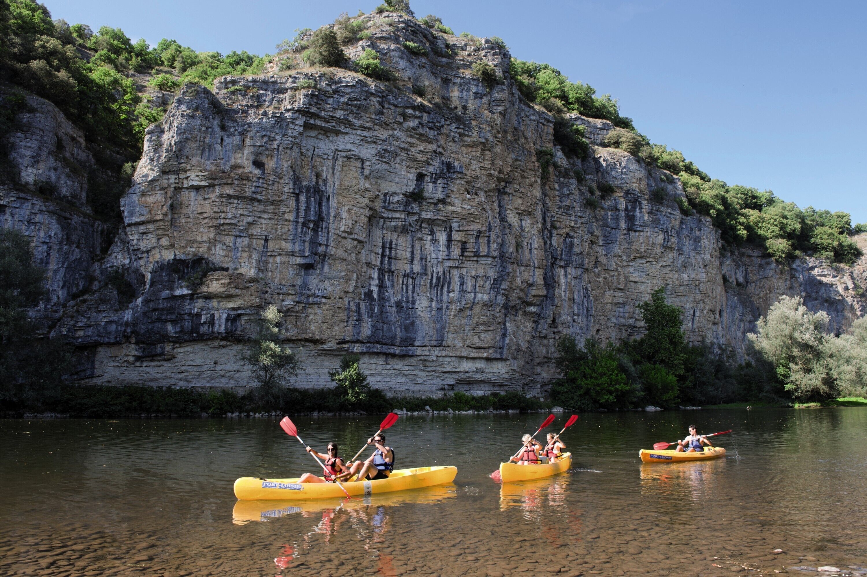 A group of people kayaking on a calm river with a large rock formation in the background.