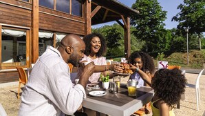 A family dining outdoors at a wooden building with large windows and a covered patio area. - Belambra Clubs Résidence Rocamadour - Les Portes De Dordogne (Alvignac)