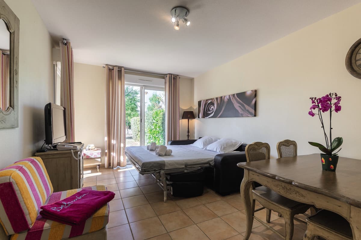Une chambre d’hôtel avec un lit, une table à manger, une télévision et une vue sur la verdure environnante.