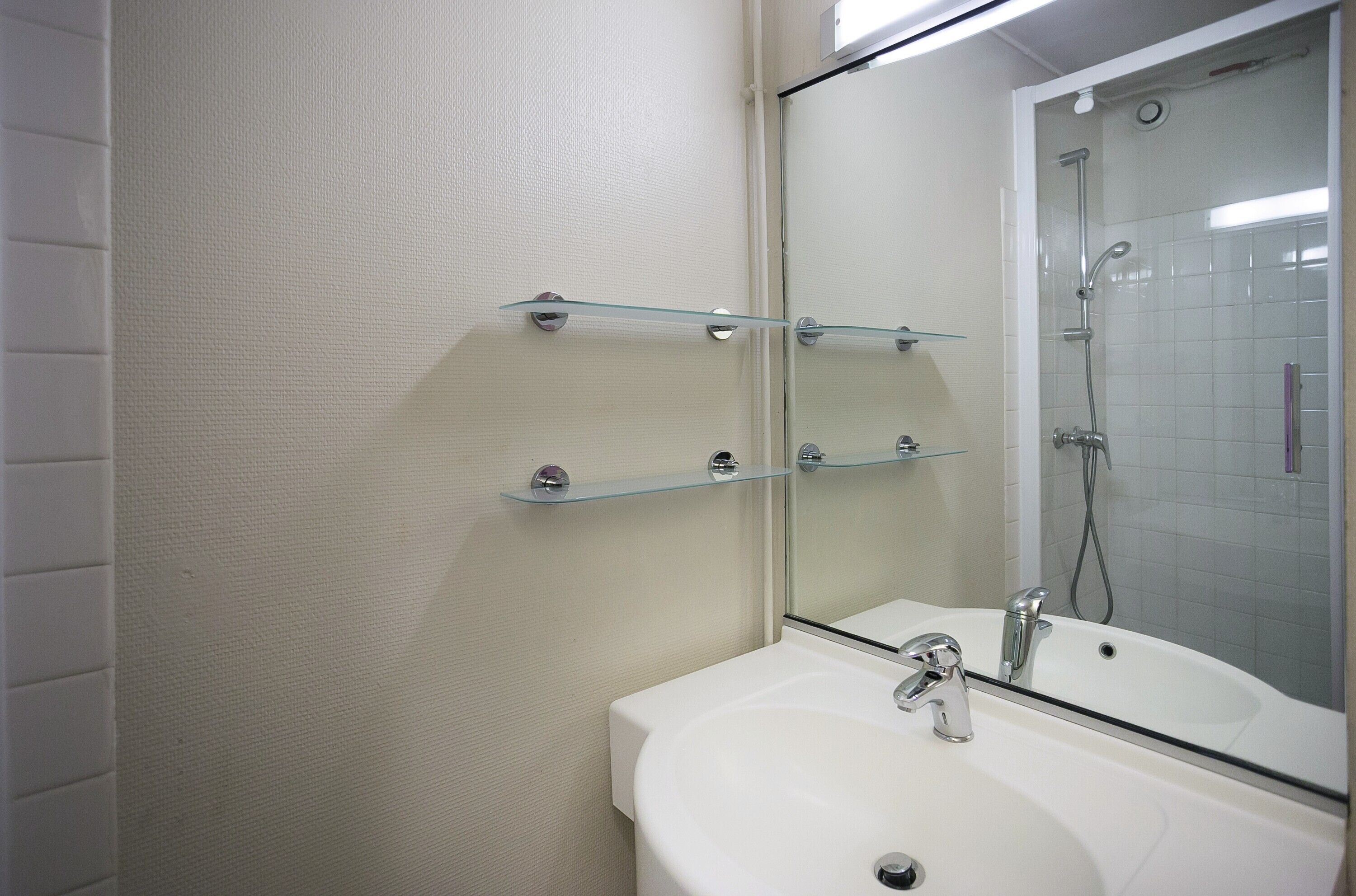 Un baño con lavamanos blanco, cabina de ducha con paredes de vidrio y tres estantes de vidrio en la pared.